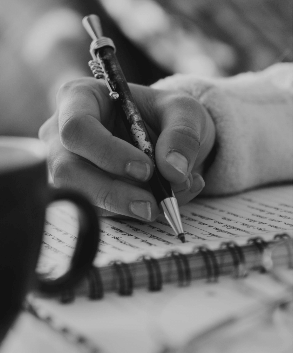 A black and white photo of a hand writing in a note book