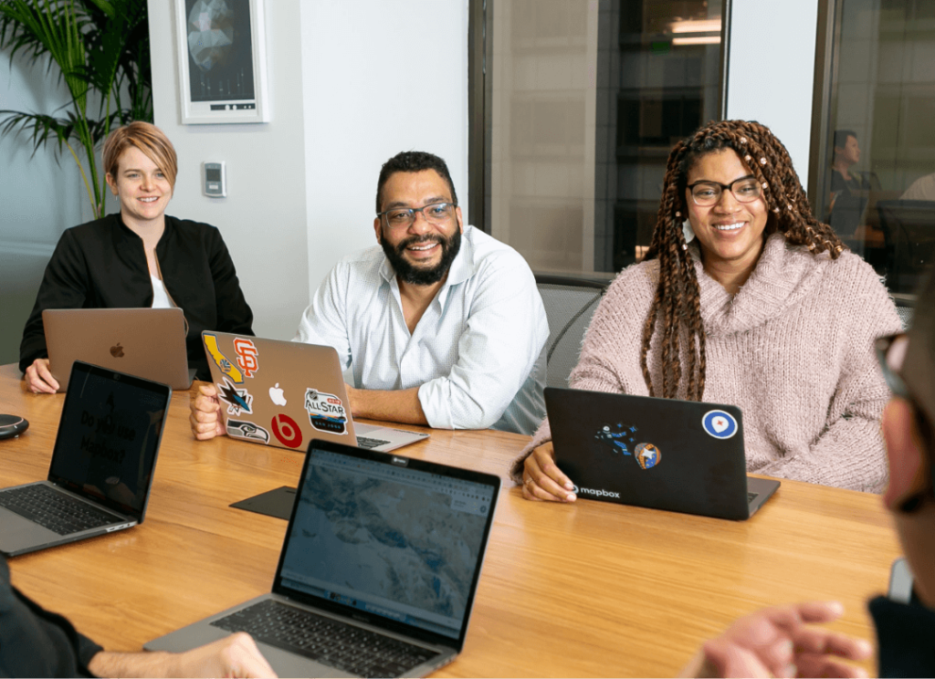 A group of people sitting at a boardroom table with laptops in front of them