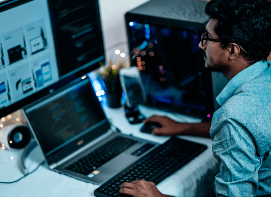 A man sitting at a computer which is hooked up to an extra monitor