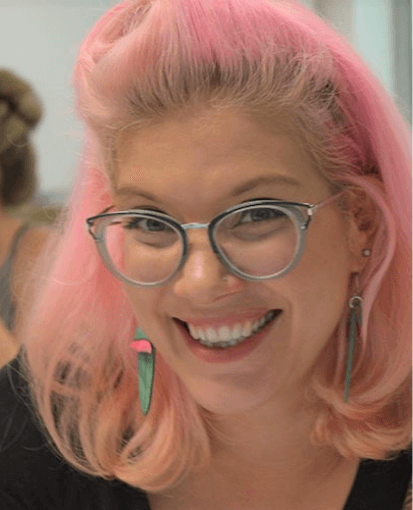 A woman with pink hair and glasses smiling