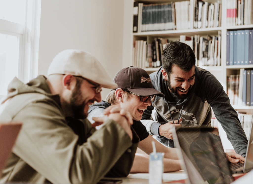 Three men laughing and all looking at the same computer